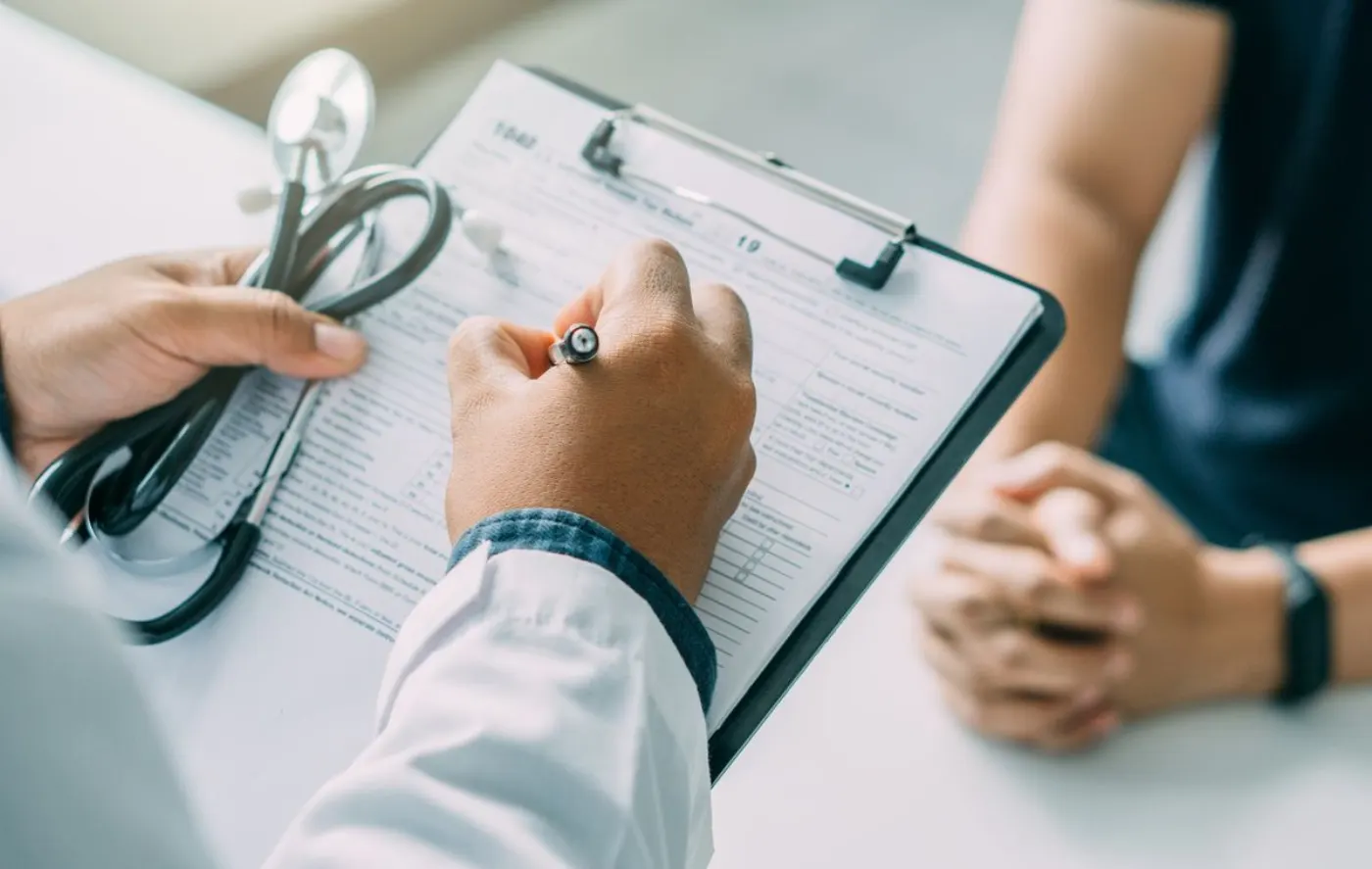 Médico a preencher um formulário clínico numa prancheta, frente a um doente