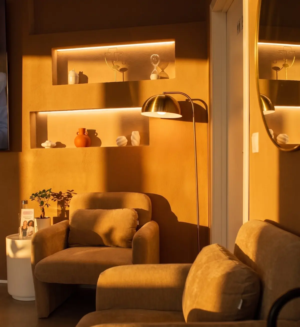 Sala de espera da clínica com cadeirões, candeeiro e luz quente ao fim da tarde